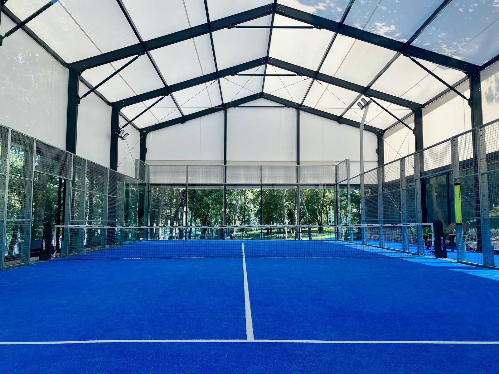 Padel court under a steel-framed canopy roof with open glazed sides