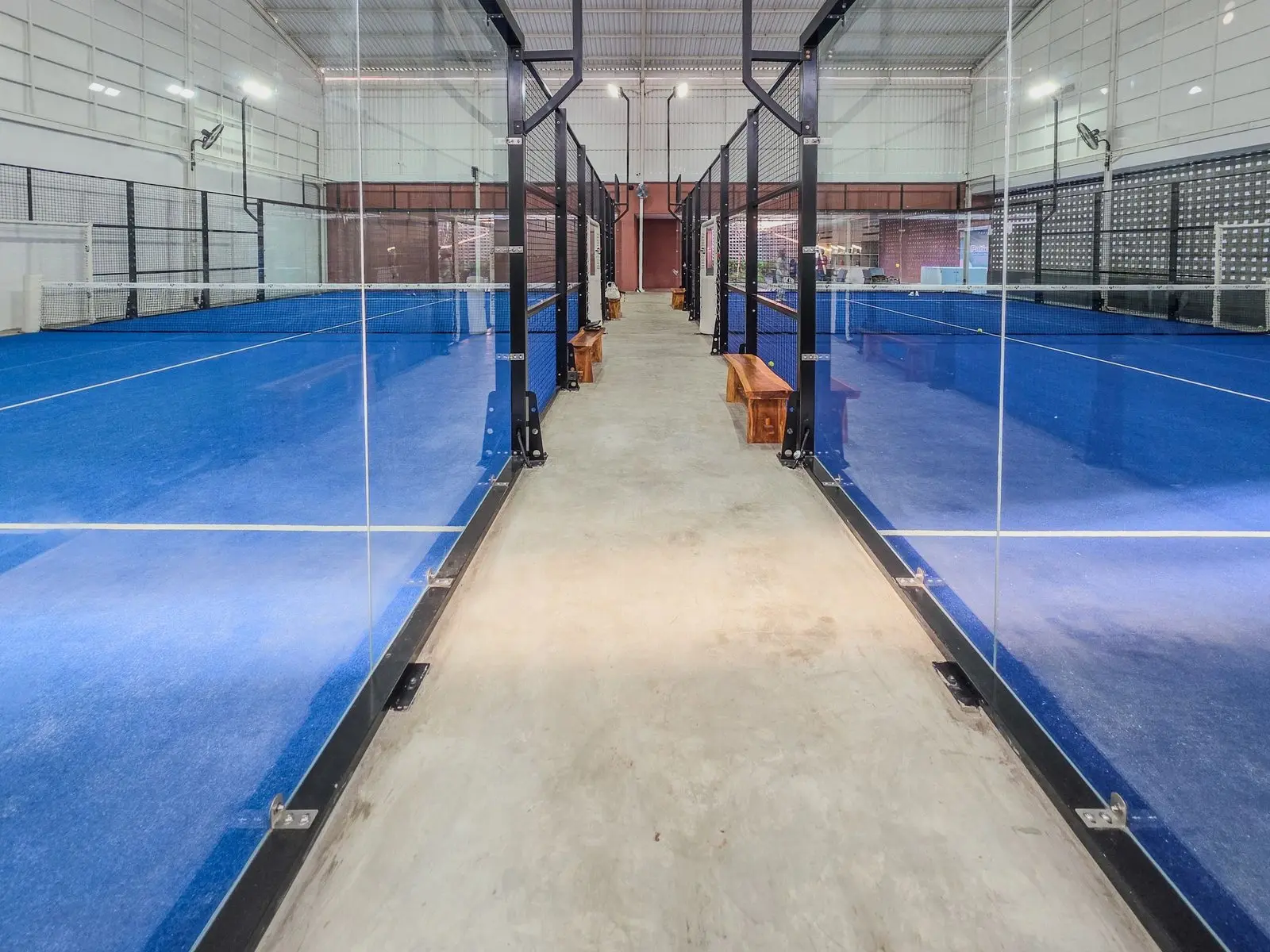 Indoor padel centre with glass-walled courts either side of a central walkway