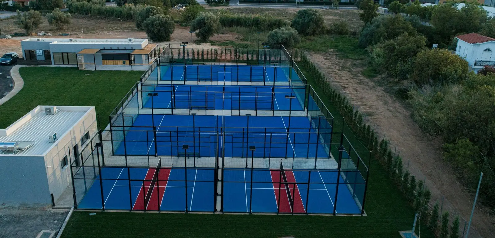 Aerial view of a padel club with five glass-walled courts beside a single-storey clubhouse