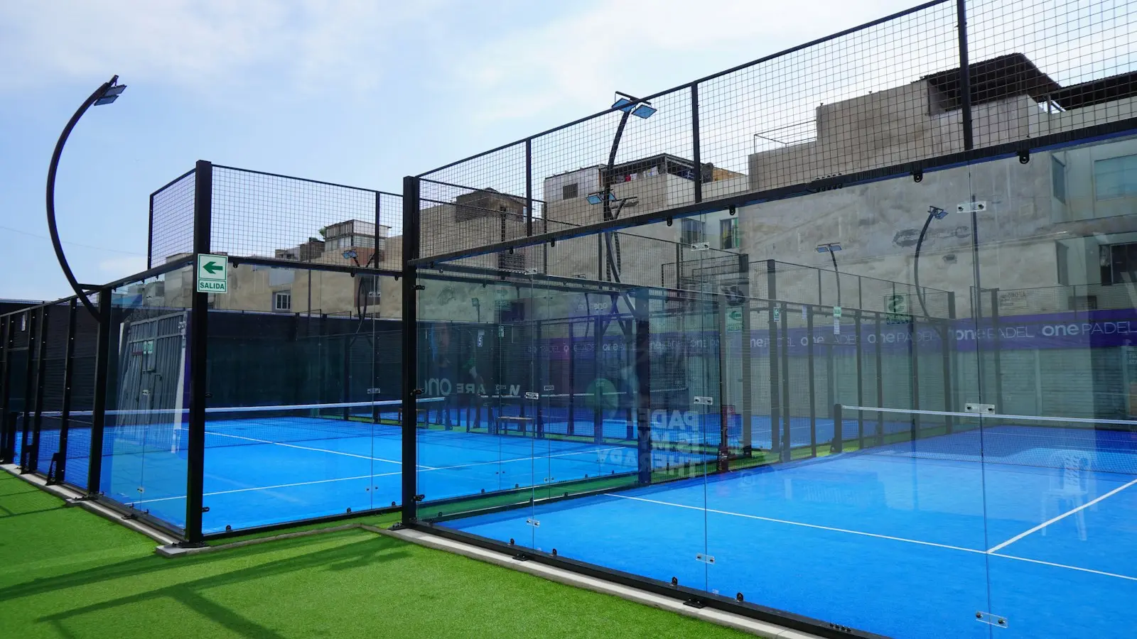 Outdoor padel courts with glass back walls, mesh panels and floodlight columns