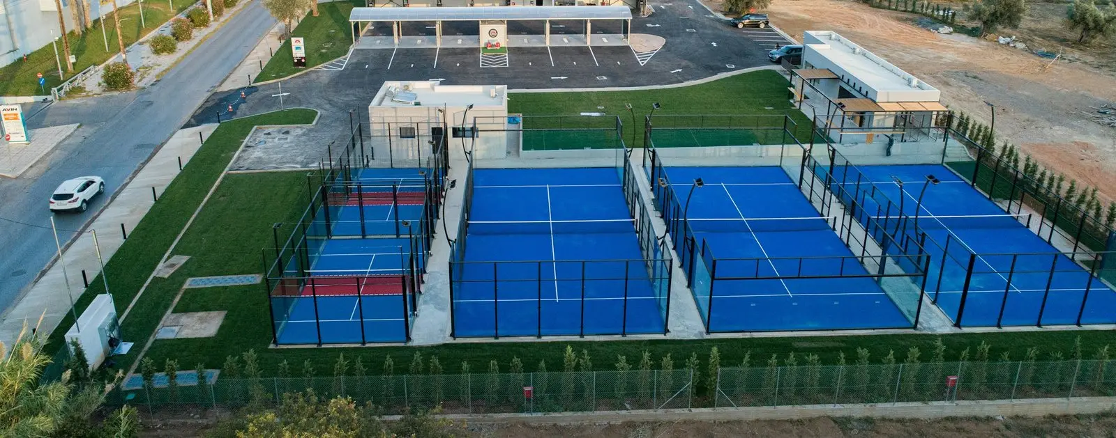 Aerial view of a four-court padel club next to a road, car park and neighbouring buildings