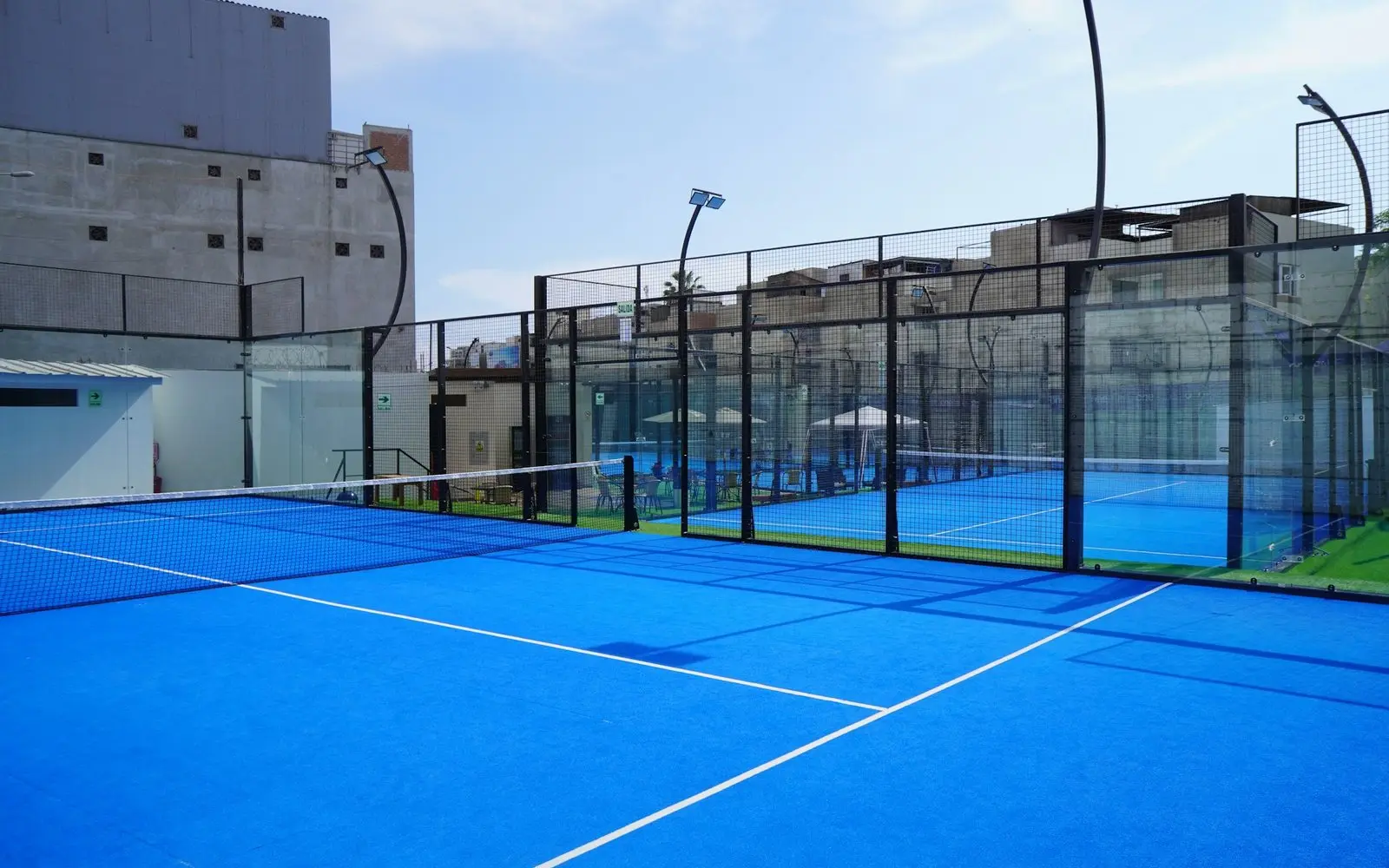 Finished outdoor padel court with glass back walls, mesh side panels and blue artificial turf