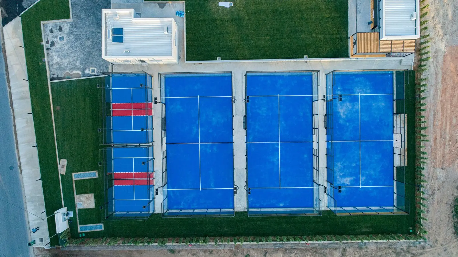 Top-down aerial view of a padel club layout: one court with red service boxes and three blue courts side by side