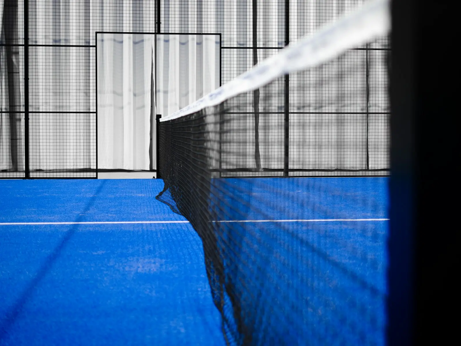 Padel court net over blue artificial turf with white court lines