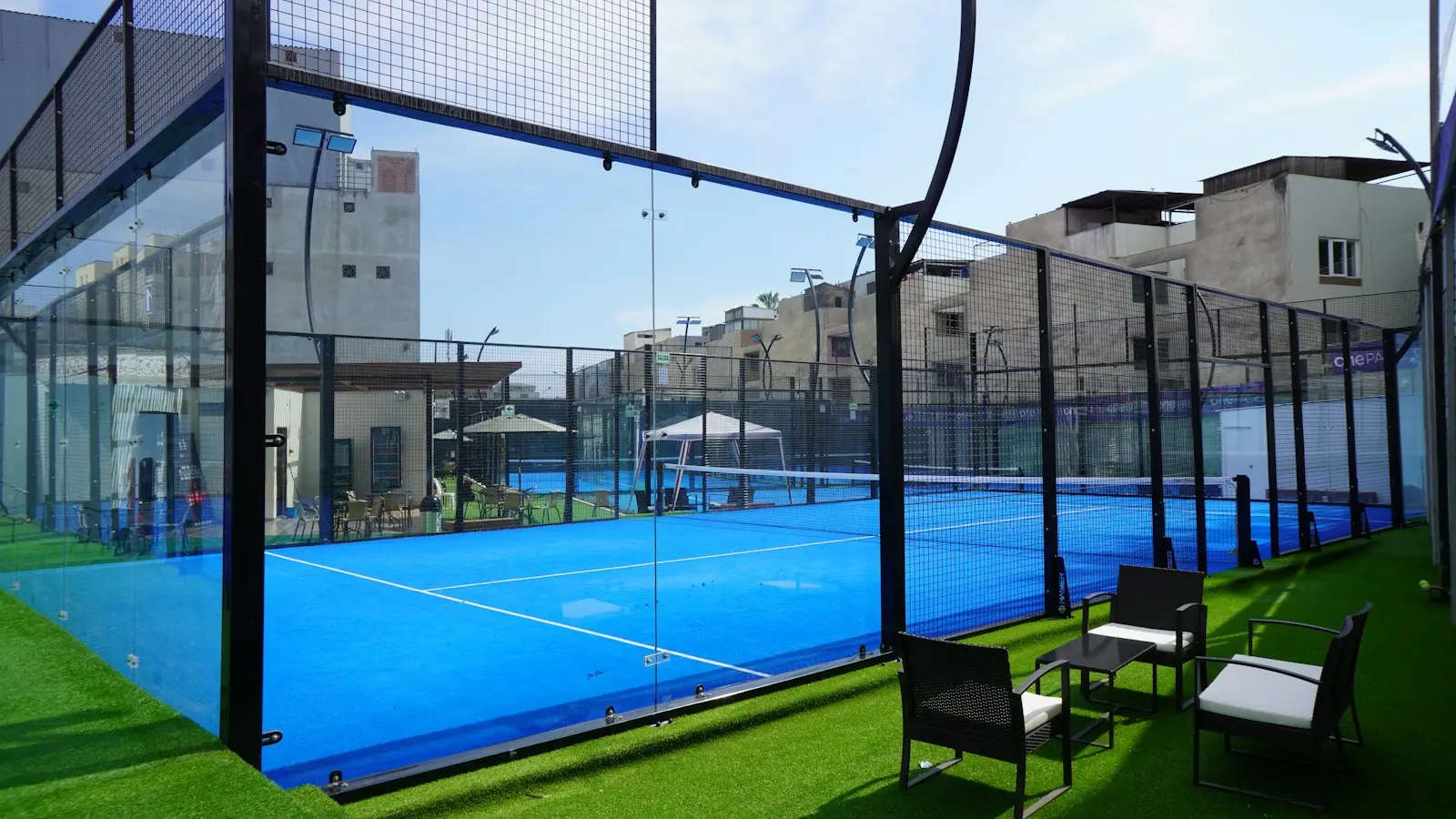 Finished outdoor padel court with glass walls and seating on the grass beside it