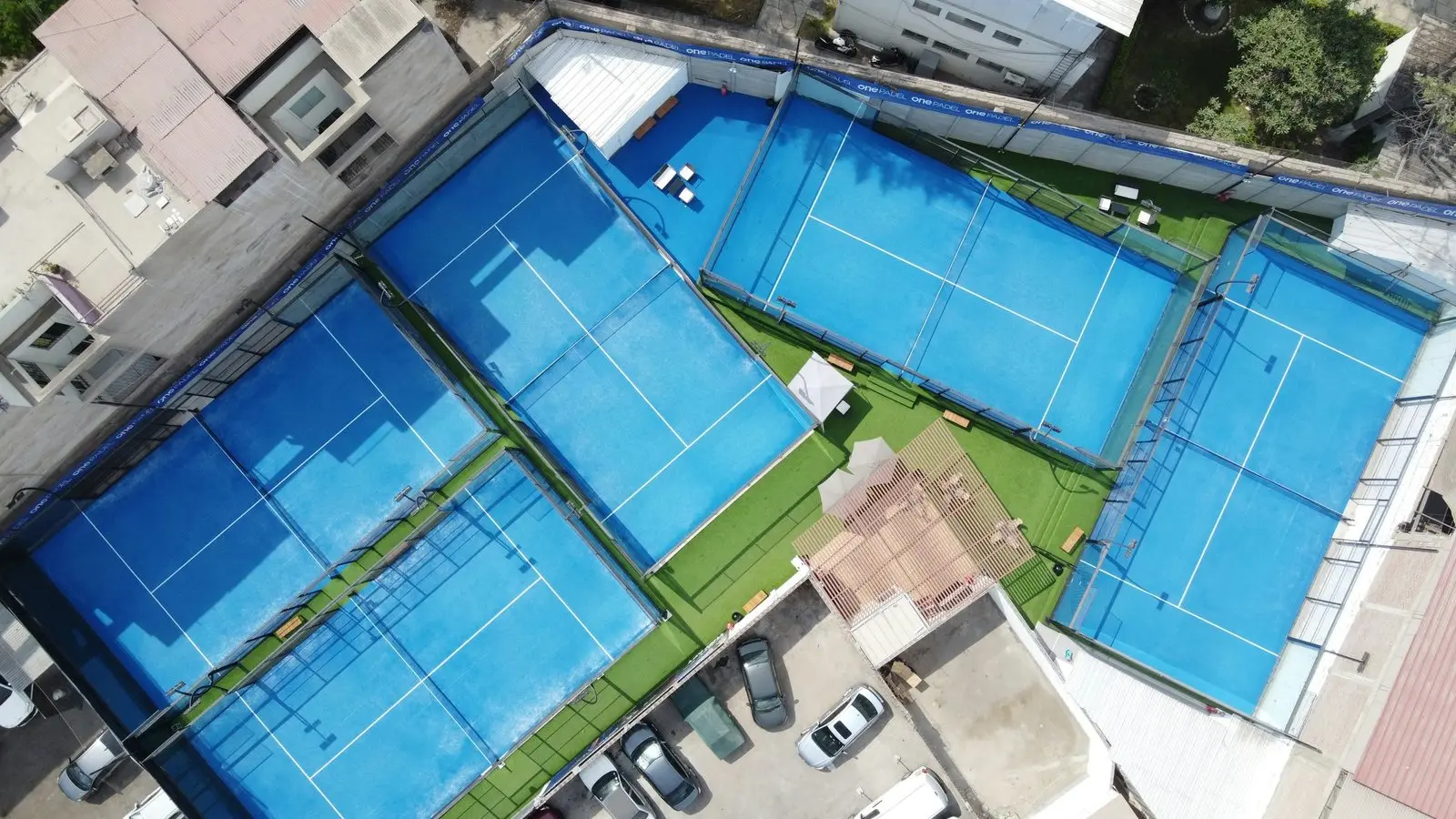Aerial view of four outdoor padel courts with glass walls and blue turf