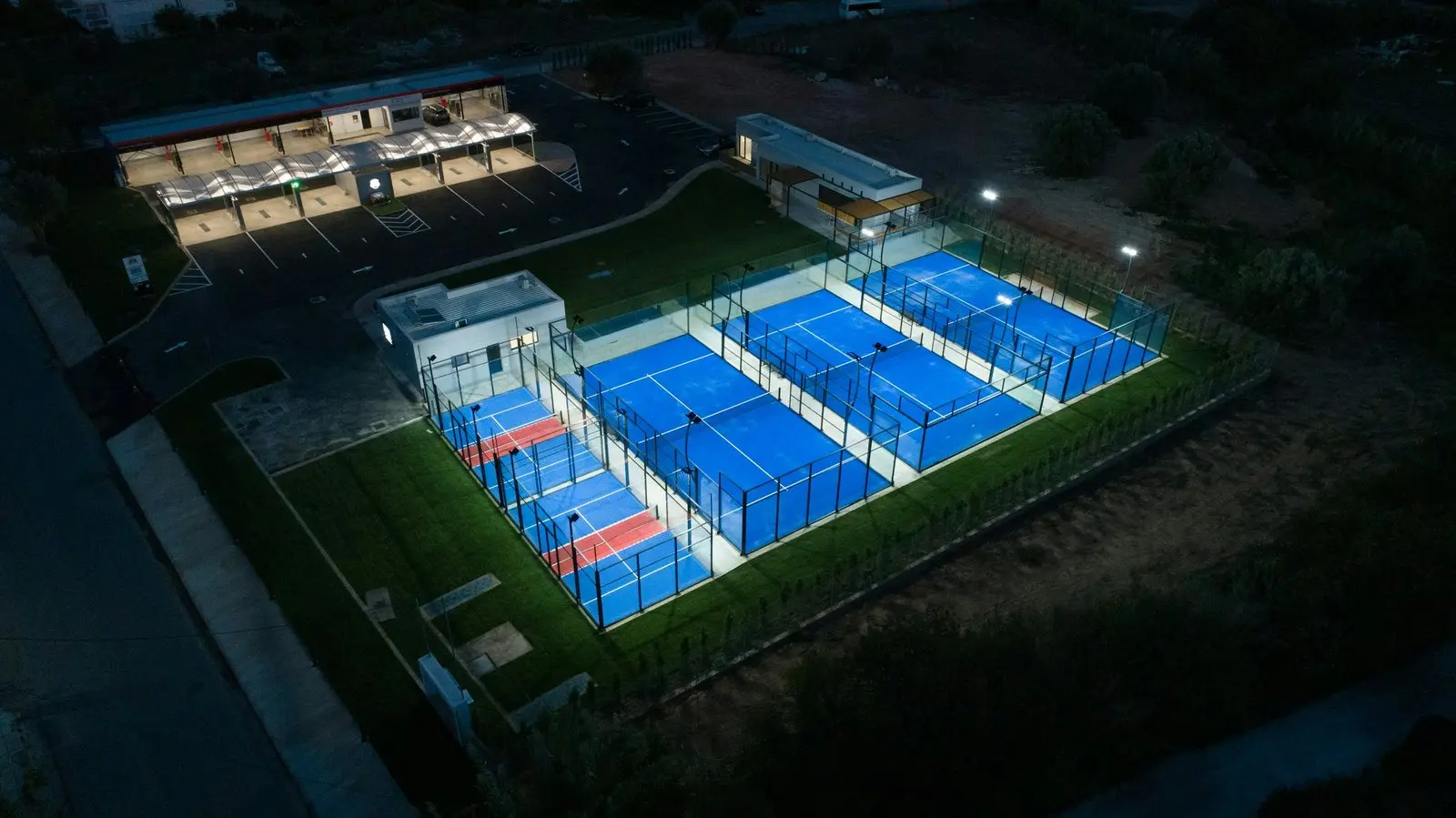 Four padel courts lit by floodlights in the evening, seen from above